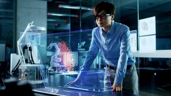亚洲神经网络工程师使用透明全息显示的现代计算机显示器显示交互式人工智能界面拍摄于现代玻璃混凝土办公室