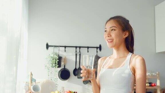 亚洲美女穿着运动服在家运动后喝水年轻的口渴活跃的运动女孩喝干净的矿物自然在杯子锻炼后保健在厨房在房子