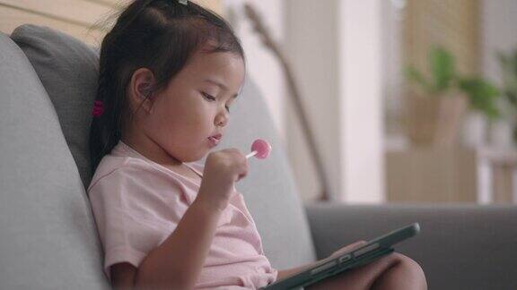 小女孩在家吃棒棒糖用平板电脑看电视
