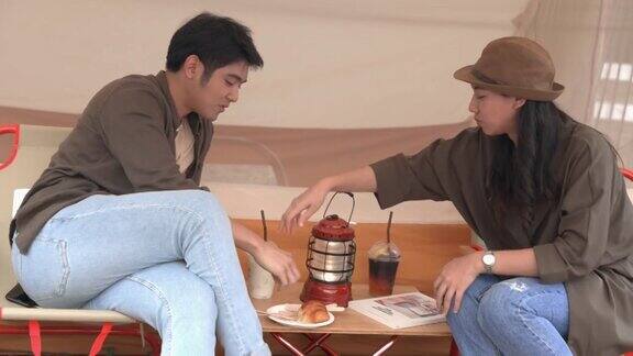 年轻的亚洲夫妇在帐篷前一起喝咖啡聊天