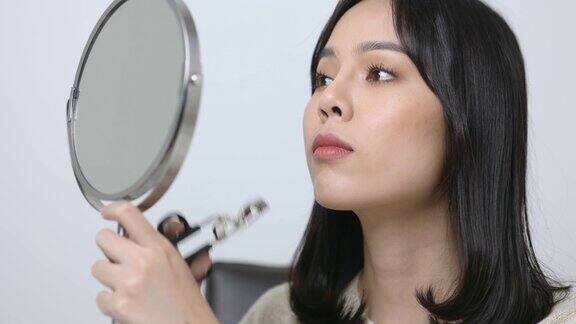 年轻的亚洲女子使用睫毛夹美丽的女人看着镜子和化妆4k决议