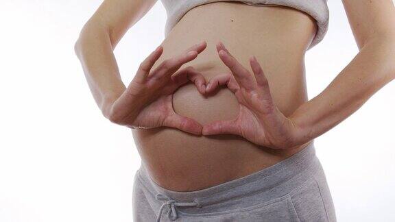一个孕妇的近距离抚摸她的腹部在缓慢的动作使一个心脏的手指在胃