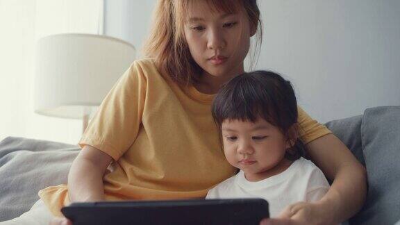 快乐快乐的亚洲家庭妈妈和可爱的孩子使用数字平板电脑兴趣卡通和看电影在家里客厅的沙发上放松