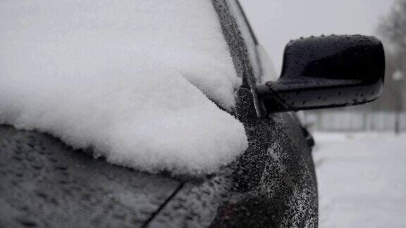 冬天雨夹雪融化在一辆现代黑色轿车的引擎盖上