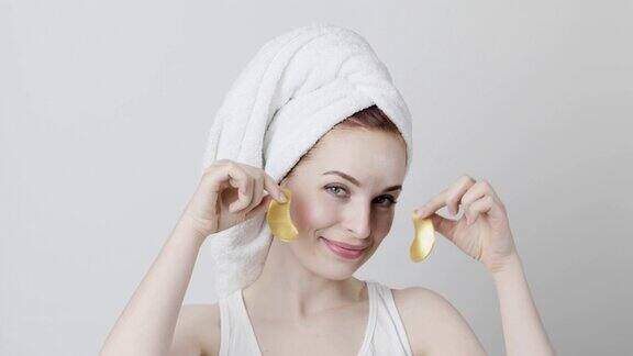 微笑的女人用毛巾包着头发双手戴着金色的眼罩