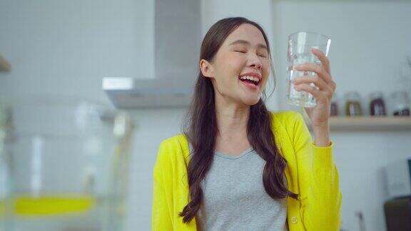 年轻的亚洲女人在厨房里微笑着喝水