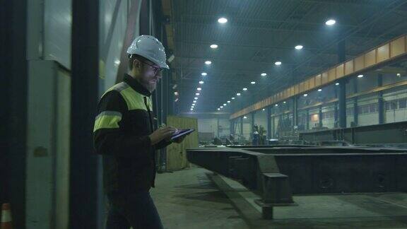 戴安全帽的工程师正带着一台平板电脑穿过一家重工业工厂