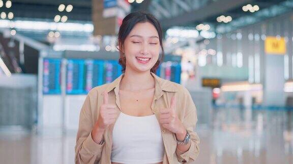 年轻微笑的亚洲妇女在公共机场航站楼竖起大拇指快乐满意的女性做手势并提供积极的服务旅游行程的旅行