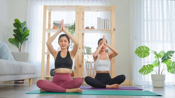 亚洲女性朋友一起在家做瑜伽普拉提迷人的女孩穿着运动服用垫子在家里的客厅里度过自由的休闲时光进行保健运动