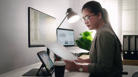 在一个被数据电脑屏幕包围的办公室里工作的亚洲女商人