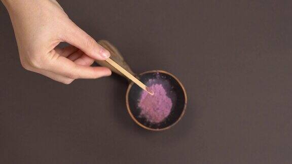 俯视图将干药草有机粉放入木碗中以灰色为背景用手将紫花粉加入碗中天然化妆品配制概念混合成分