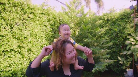 快乐的亚洲家庭妈妈背着可爱的小宝贝孩子蹒跚学步的女孩在公园里跳舞玩耍一起微笑着无忧无虑的妈妈和女儿的爱照顾关系