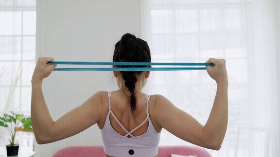 背面的亚洲运动妇女是使用阻力带手臂锻炼建立肌肉