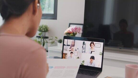 年轻的亚洲女商人使用笔记本电脑在视频电话会议上与同事谈论计划而在家中的客厅工作