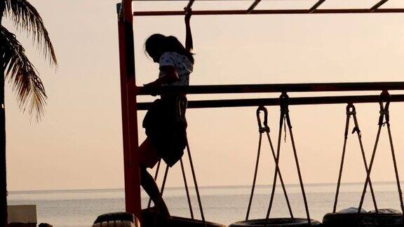 女孩的剪影在海滩附近玩攀岩器材的早晨生活方式