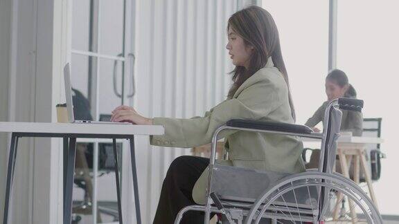 年轻的女商人坐在轮椅上快乐地工作平衡地工作和生活坐在轮椅上的妇女使用笔记本电脑在办公室工作平等概念