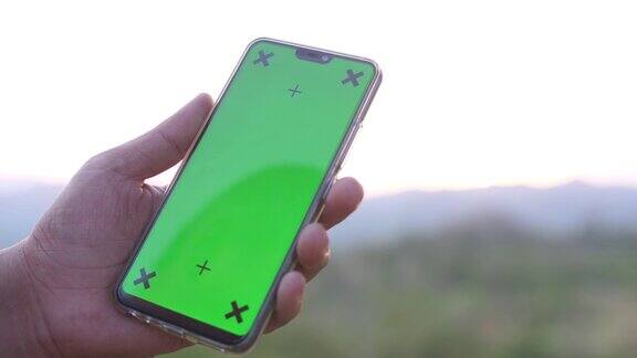 手持绿色屏幕和自然背景的智能手机色度键