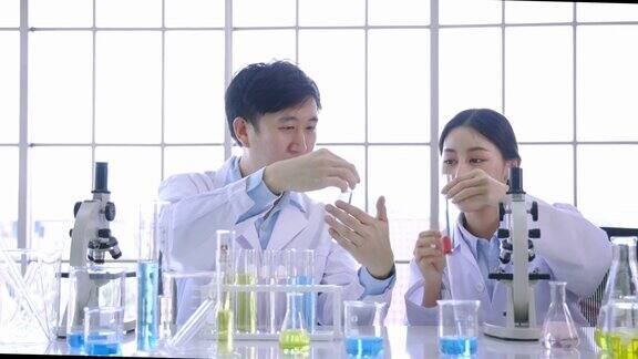 年轻的亚洲女性和男性同事科学家在生命科学研究实验室使用显微镜和拿着试管
