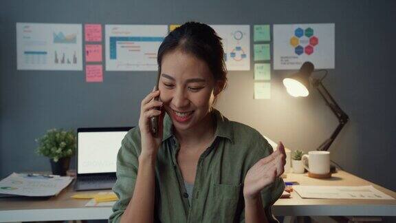 快乐年轻的亚洲商业女性自由职业者使用智能手机与朋友或客户在办公室的晚上