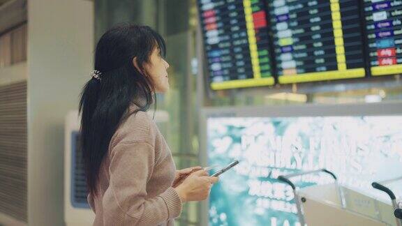 亚洲女商人手持护照和登机牌在国际机场查看航班信息板查询她的航班