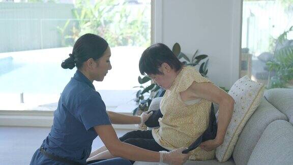 家庭护理人员在家访期间为亚洲老年妇女放回支撑带