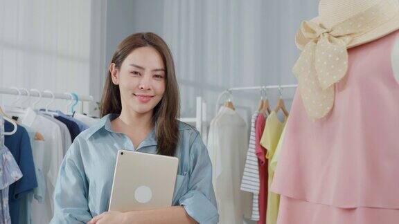 亚洲女人的肖像在网上卖衣服和看着相机有吸引力的年轻女商人使用平板电脑或笔记本电脑检查销售订单并感到高兴的财务业务在仓库