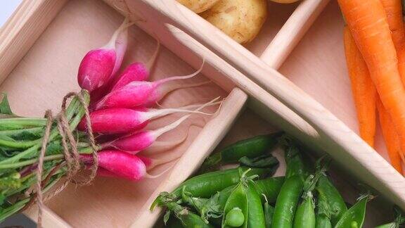 新鲜的蔬菜在木篮子里轮转绿色的豌豆、萝卜、土豆和胡萝卜特写白色背景上的俯视图