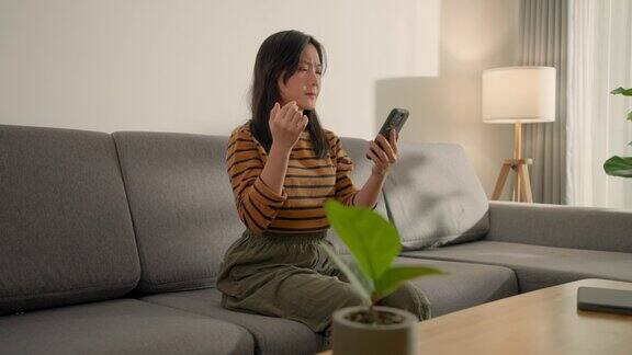 一名使用智能手机的亚洲妇女坐在家里的沙发上眼睛疼