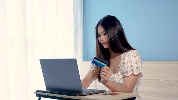 4K50fps美丽的亚洲女孩穿着白色花衬衫带着快乐的表情成功地通过笔记本电脑在线购物后网上购物