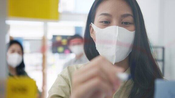 亚洲年轻的商人们讨论商业头脑风暴会议一起分享数据带着医用口罩在办公室里写玻璃墙