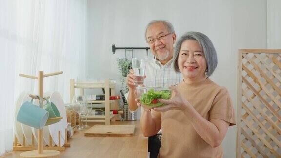 亚洲老年夫妇的肖像在家里的厨房里拿着沙拉幸福的家庭有魅力的年长成熟的丈夫和妻子享受健康的食物然后微笑一起在家里看镜头
