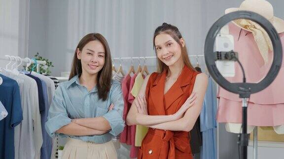 两名亚洲美女的肖像后自信地站在镜头前卖衣服年轻有魅力的商务人士通过虚拟在线直播工作看着镜头
