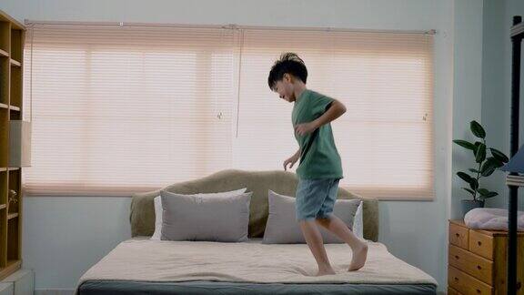 4K慢亚洲男孩英俊男孩穿着一件绿色的t恤他在床上跳上跳下一直跳他高兴地跳跺着脚独自在卧室里不觉得累