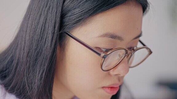 戴眼镜的亚洲女性在家学习在笔记本上写字远程教育
