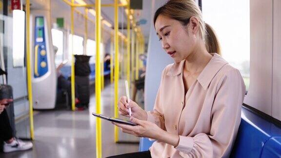 近距离的亚洲商业女性通勤与铁路运输同时工作和书写的数字平板电脑在去办公室
