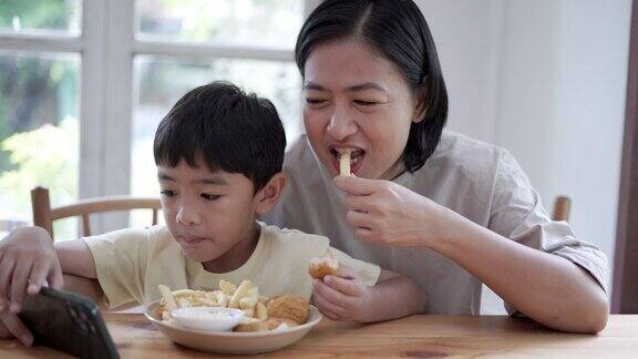 小男孩一边吃薯条一边看手机