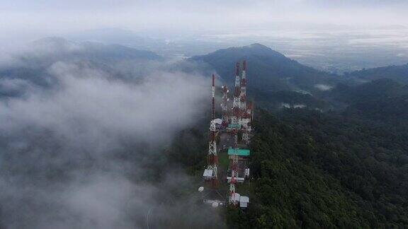 无人机电影鸟瞰图在多云的早晨在白色云海之上的山顶上的电信塔与雾