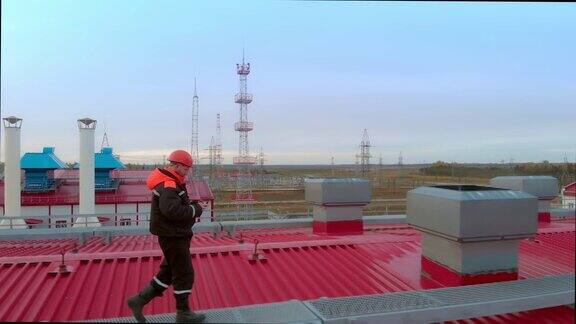 一名石油和天然气工人戴着橙色的工作头盔穿着低温工作服绕过一个使用燃气轮机的燃气电厂危险的工作
