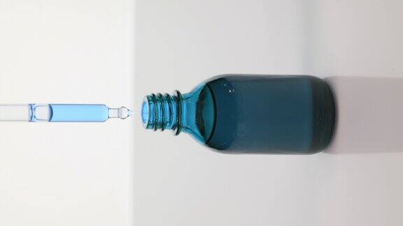 滴管将蓝色油滴入灰色背景的蓝色瓶中