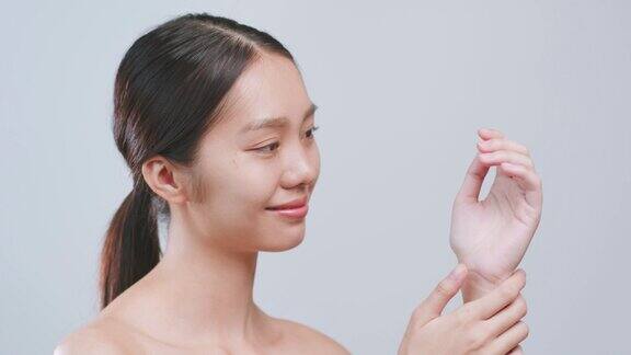 肖像年轻的亚洲美女应用手霜和乳液在灰色的背景亚洲美容皮肤