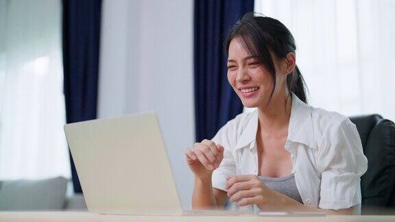 快乐的年轻亚洲女性在笔记本电脑上庆祝赢得或获得电子商务购物优惠兴奋快乐的女孩赢家看着笔记本庆祝成功