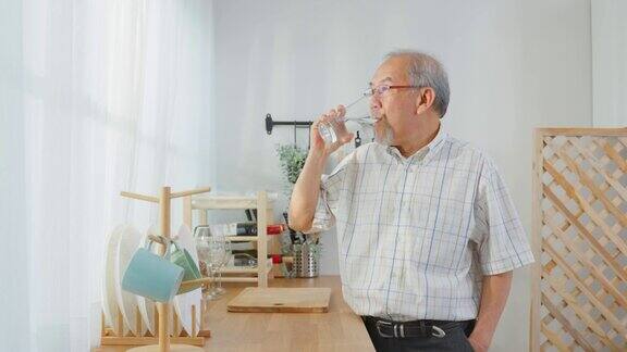 亚洲资深成熟男性在家里的厨房喝一杯水有吸引力的老人年长的爷爷拿着清洁的矿物自然在杯子和睡眠在早上的健康幸福在家里