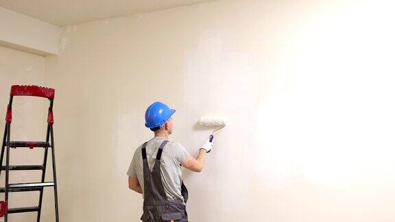 穿着工作服的建筑工人用滚筒把墙刷成白色