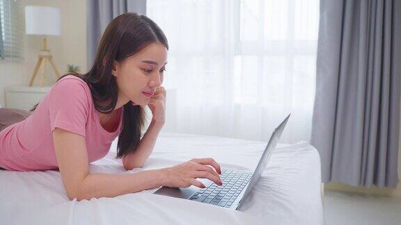 亚洲迷人的女人用笔记本电脑聊天在家里的床上早上快乐的休闲美丽的女性躺在卧室享受假期周末使用笔记本电脑与技术在家里在线交流