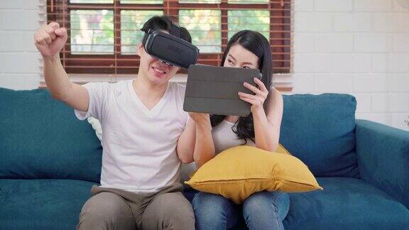亚洲情侣在客厅用平板电脑和虚拟现实模拟器玩游戏情侣们一起躺在家里的沙发上享受快乐时光生活方式家庭放松居家理念
