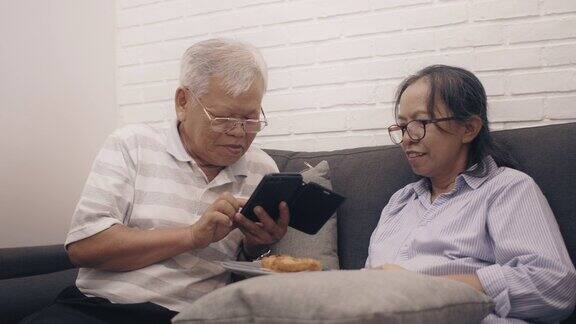 周末度假时亚洲的老夫妇在家里的卧室里用智能手机阅读社交媒体老年人幸福生活
