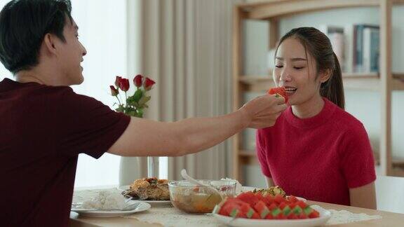 一位年轻的亚洲男子正在挑选一块西瓜给他的女朋友吃同时在家里一起享受午餐