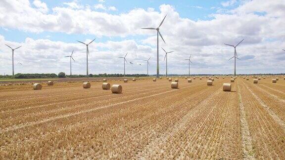 在高空摄像机记录了风力涡轮机在林肯郡农民的田地里优雅地旋转的宁静场景那里最近收获了金黄色的干草捆