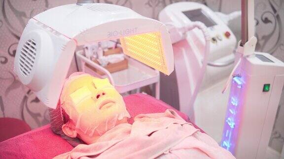 一名亚洲女子躺在床上在美容诊所使用led面膜pdt光疗