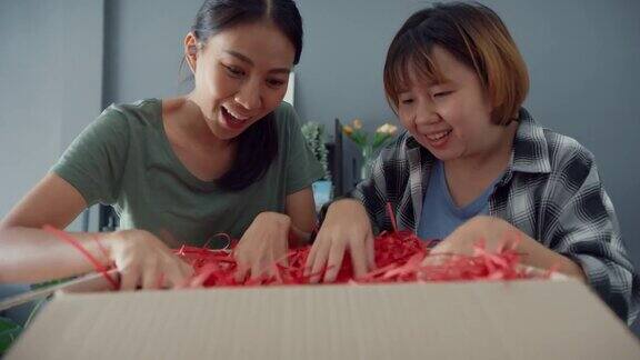 快乐的亚洲年轻女士朋友们在家里的客厅打开网上市场的快递包裹